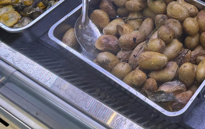Des pommes de terre grenaille rôties dans un plat inox de la vitrine du traiteur, à côté d'une poêlée de courgettes