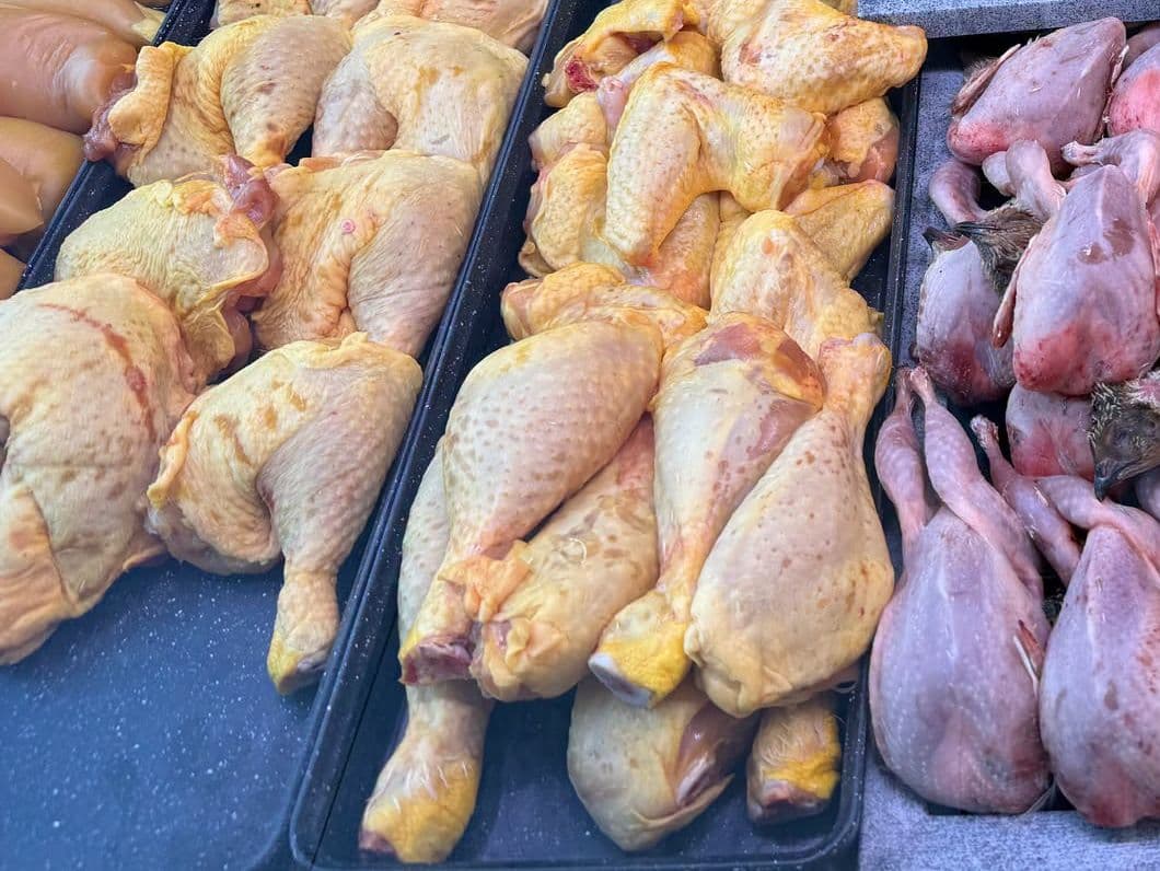 Des cuisses de poulet à la peau jaune et des volailles entières alignées dans les bacs du comptoir